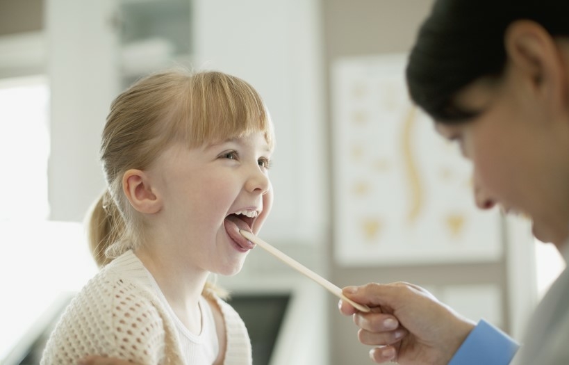 Der Mundbereich eines Kindes wird von einer Logopädin mit einem Stäbchen untersucht.